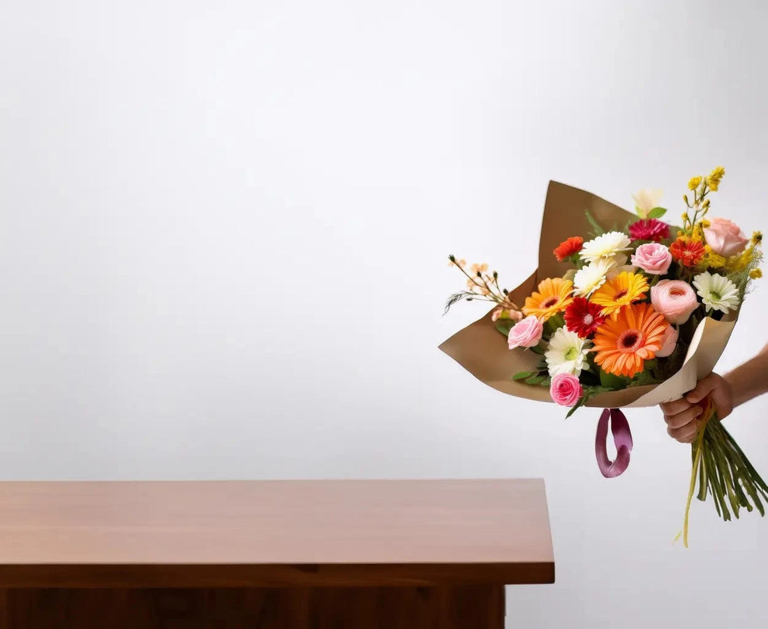 Bouquet of flowers being held above a wooden table with a plain background