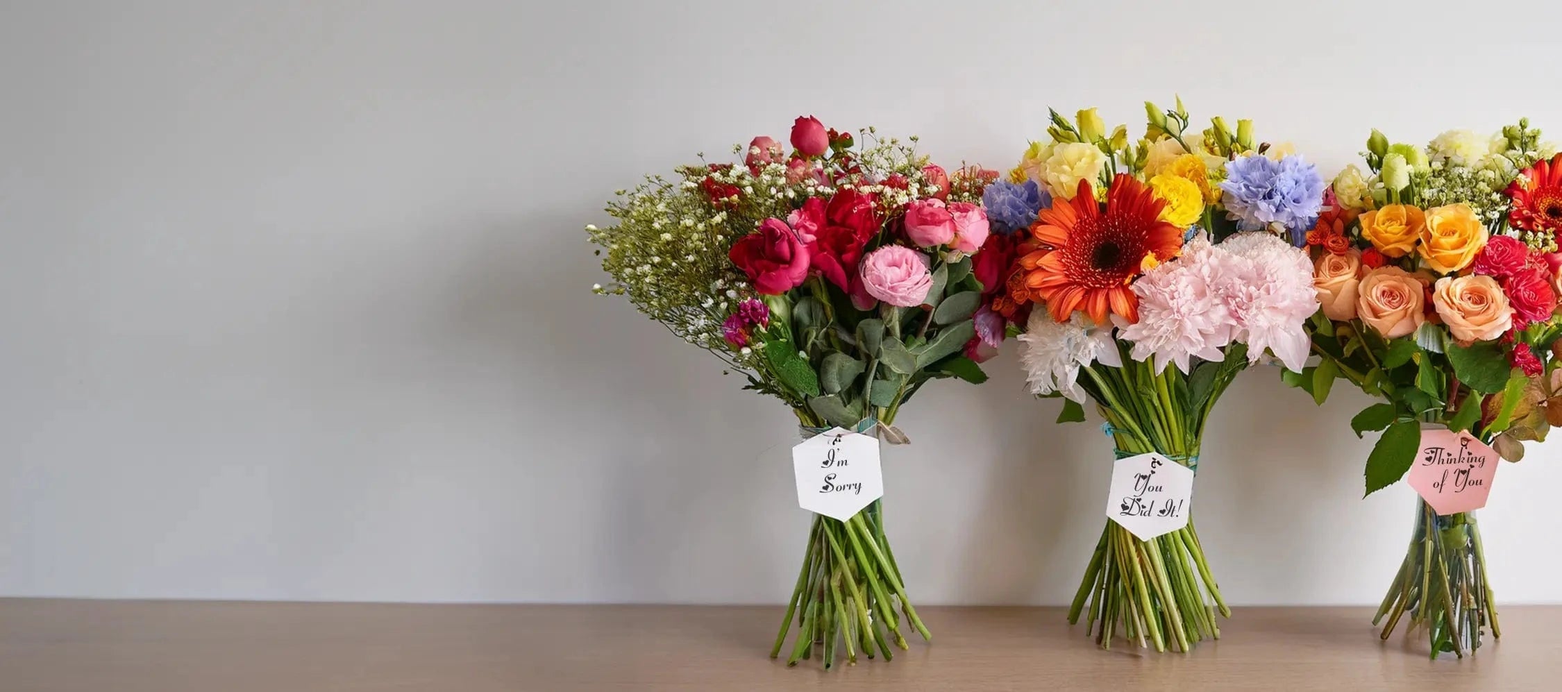 Three colorful flower bouquets on a wooden surface with a plain background