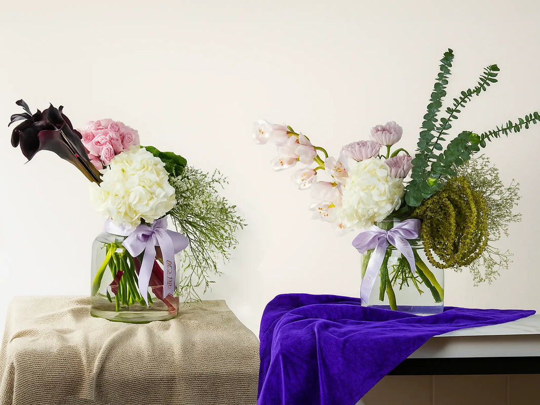 Two floral arrangements in glass jars with ribbons on a white background