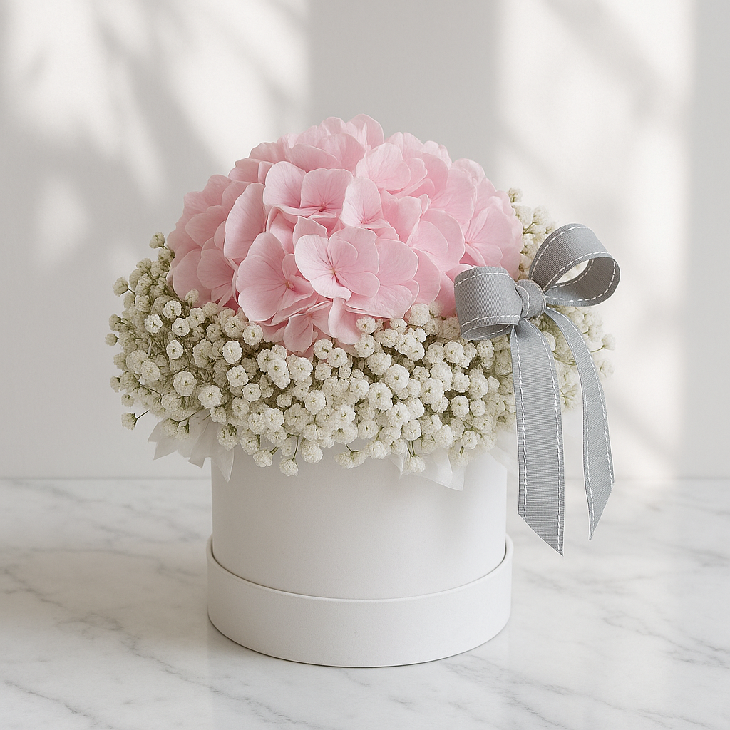 Floral arrangement with pink flowers and a gray ribbon in a white box on a marble surface.