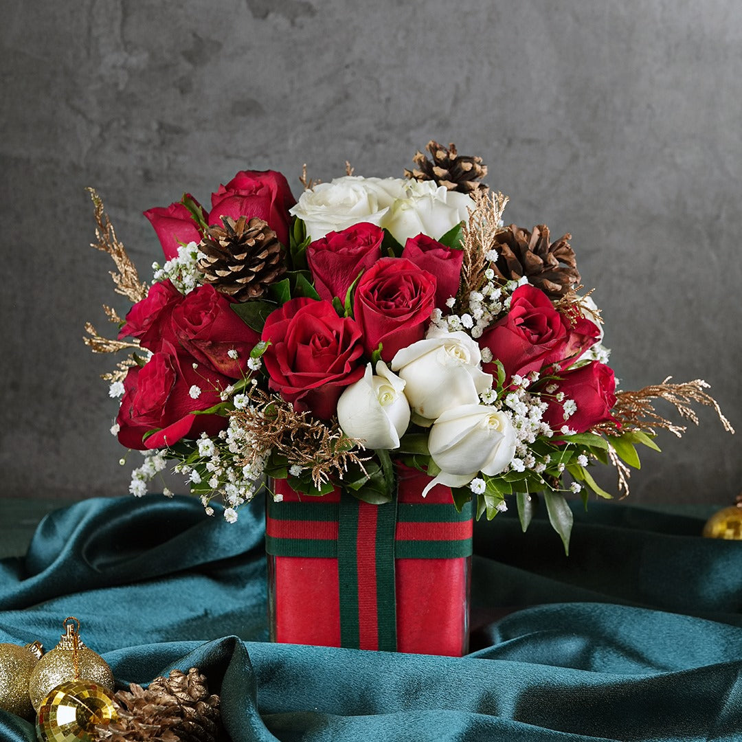 Bouquet of red and white flowers with pinecones in a decorative box on a dark fabric background.