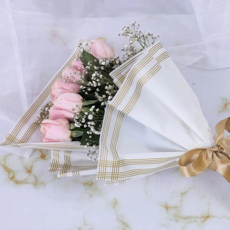 Bouquet of pink roses wrapped in white paper with gold ribbon on a marble background.