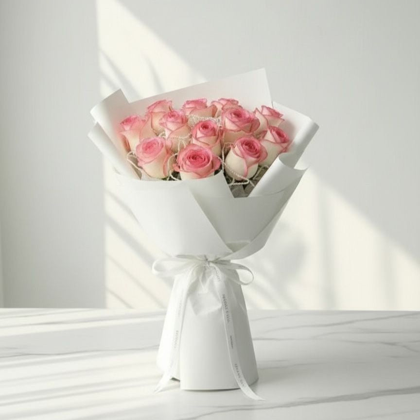 Bouquet of pink roses wrapped in white paper with a bow on a white surface.
