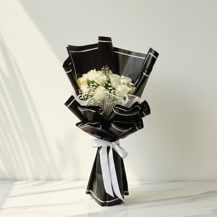 Bouquet of white roses with baby's breath wrapped in black paper and a white ribbon on a light background