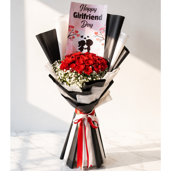 A flower bouquet for a 'Happy Girlfriend Day' gift, featuring a large cluster of red roses, baby's breath, and a pink greeting card, wrapped in black, white, and red paper with a red ribbon, set on a marble surface against a white wall.