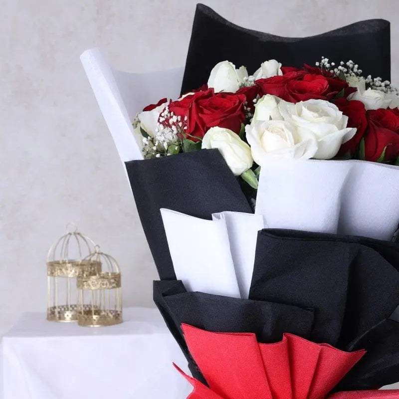 Bouquet of red and white roses with a decorative birdcage on a white surface.