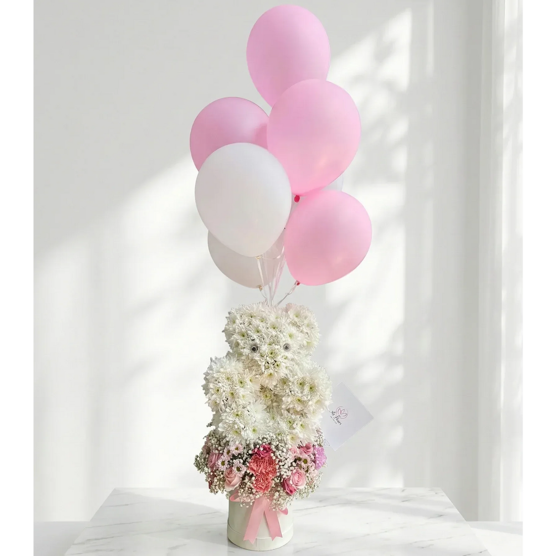 Bouquet of flowers with pink and white balloons on a marble surface.