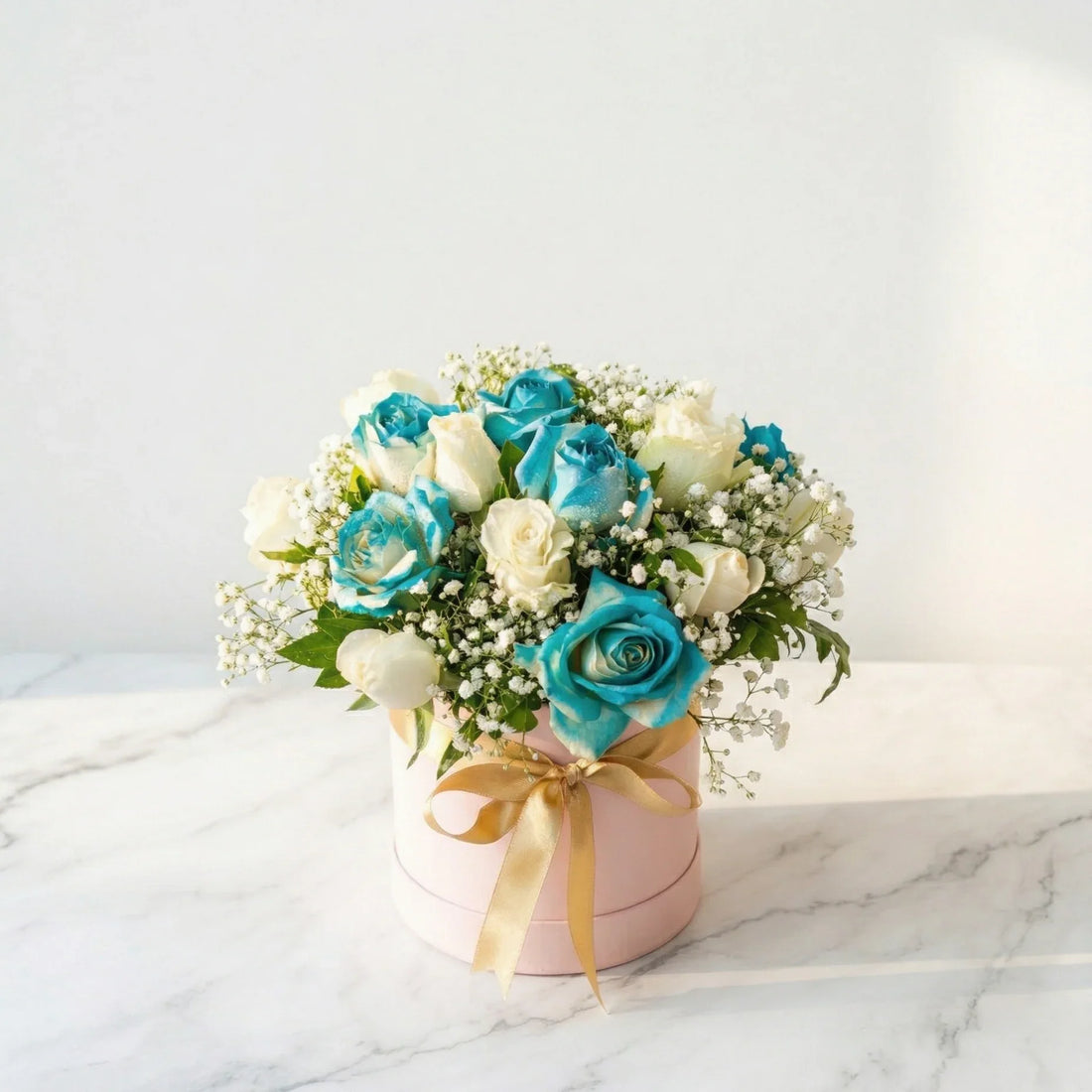 Bouquet of blue and white roses in a pink box on a marble surface with a light gray background