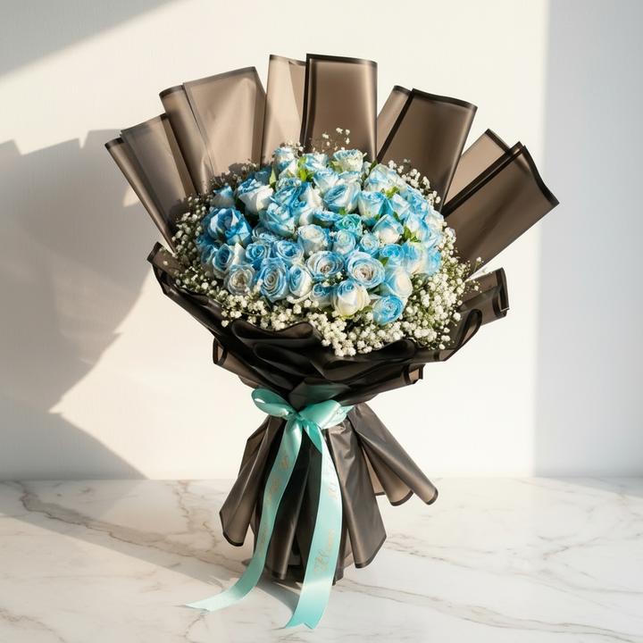Fresh light blue and white roses with gypsophila baby's breath wrapped in matte black frosted paper with a mint green ribbon by At Fleurs Bandra Mumbai