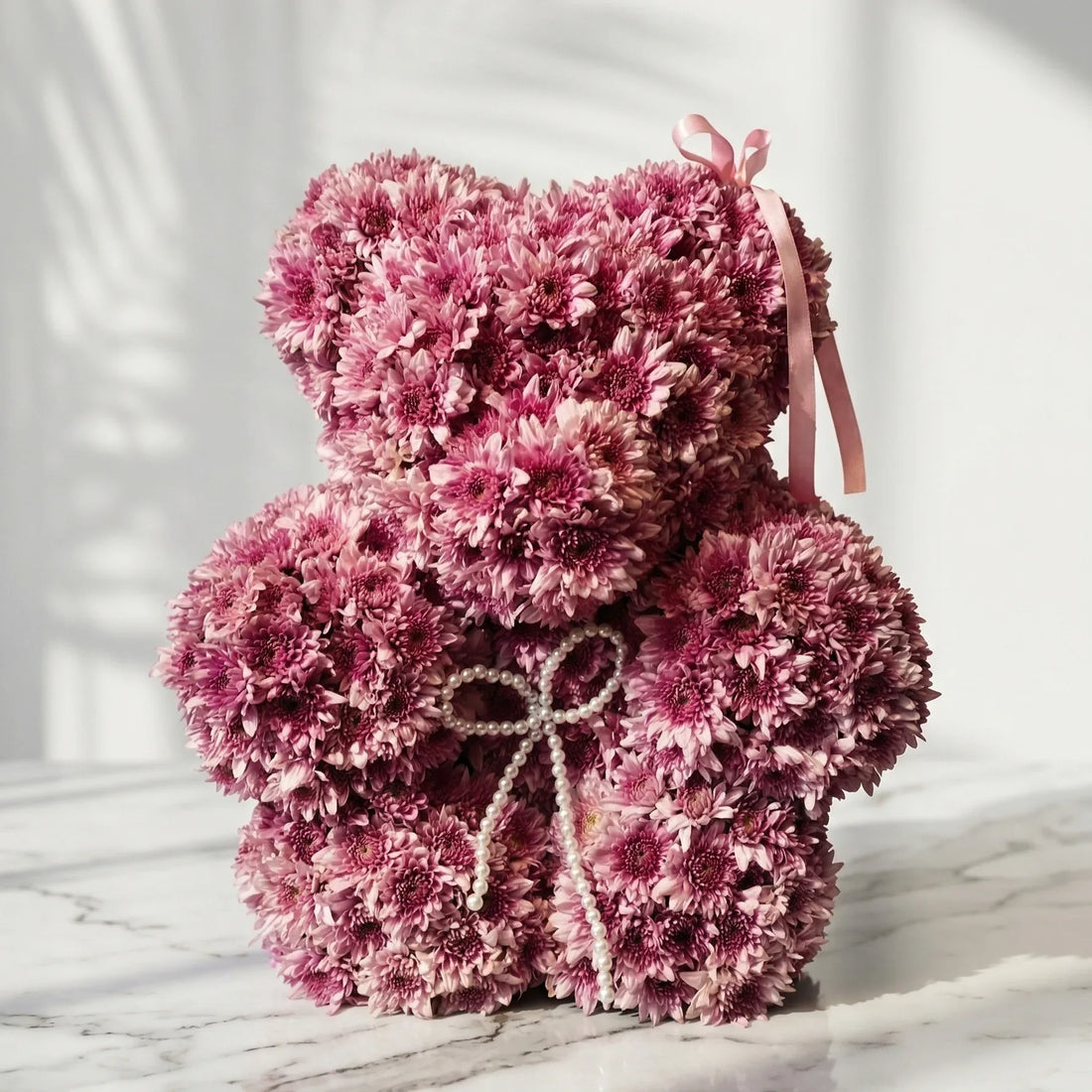 Teddy bear made of pink flowers on a marble surface with a white background