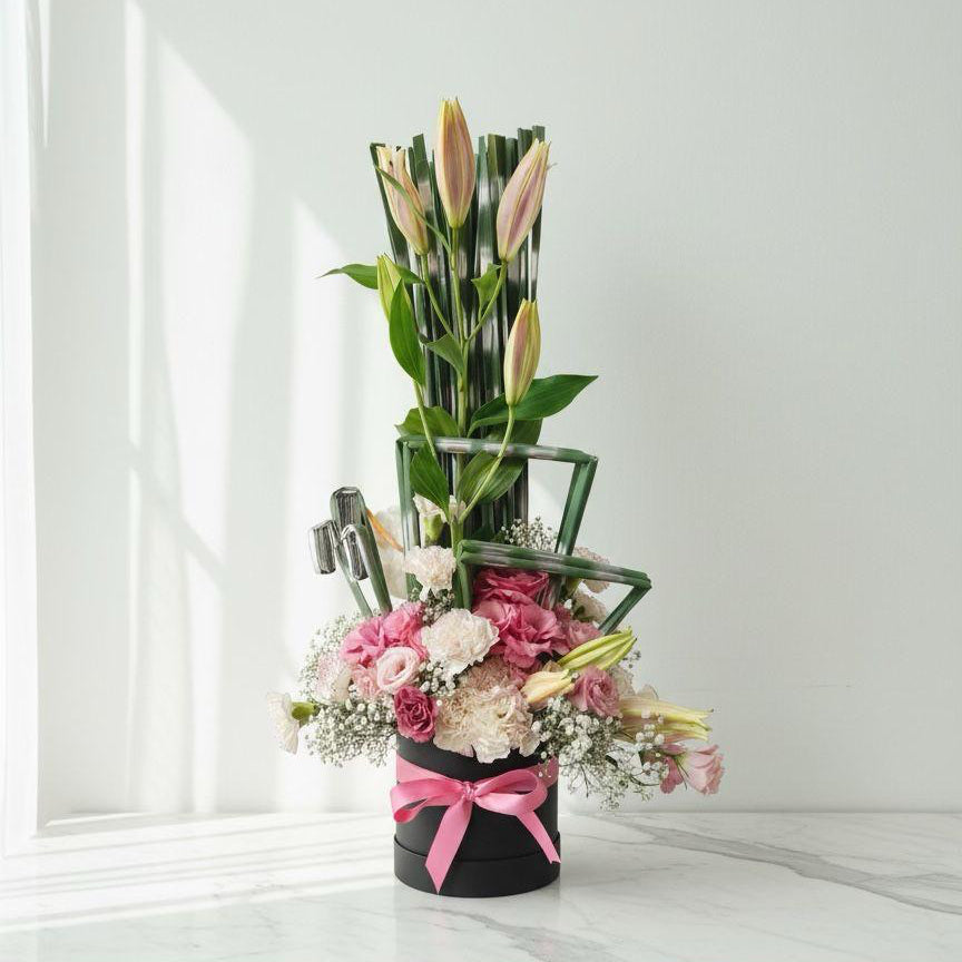 Floral arrangement in a black vase with a pink bow on a white surface.