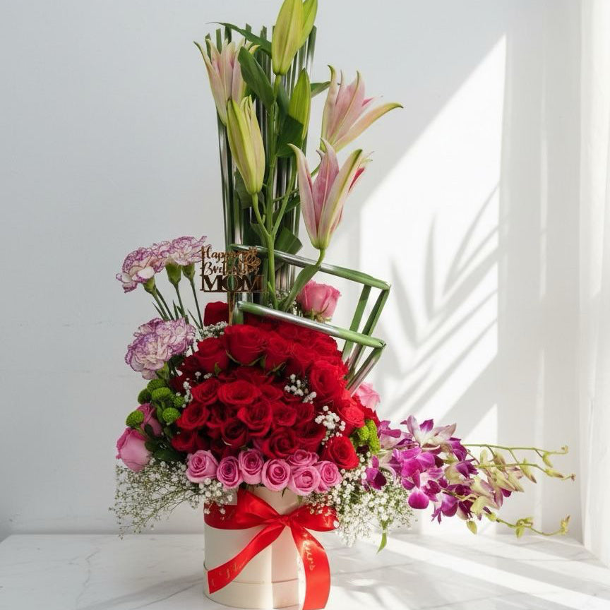 Bouquet of flowers with red roses, pink tulips, and greenery on a white surface.