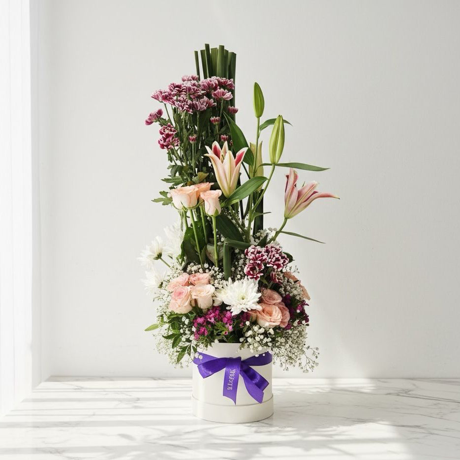 Floral arrangement in a white container with a purple ribbon on a light background