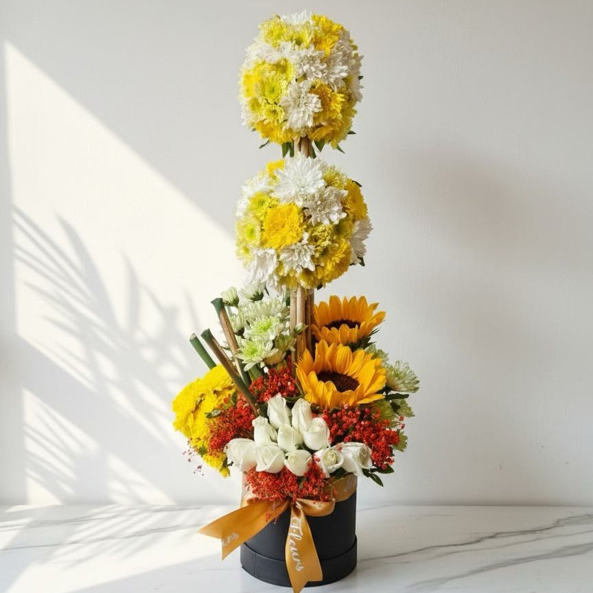 Floral arrangement with yellow, white, and red flowers in a black pot on a light surface.