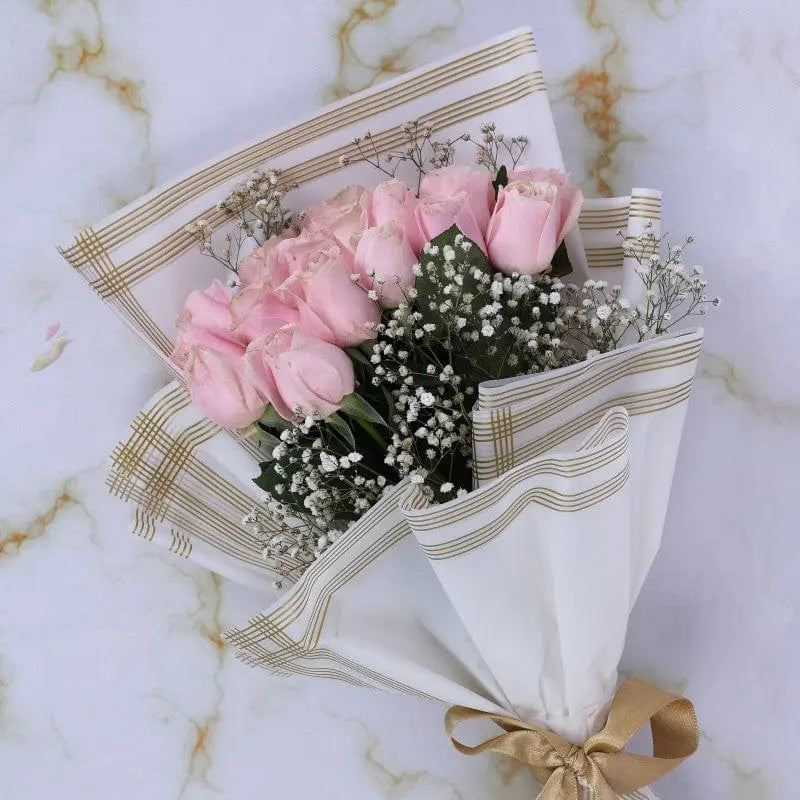 Bouquet of pink roses wrapped in white paper with gold ribbon on a marble background.
