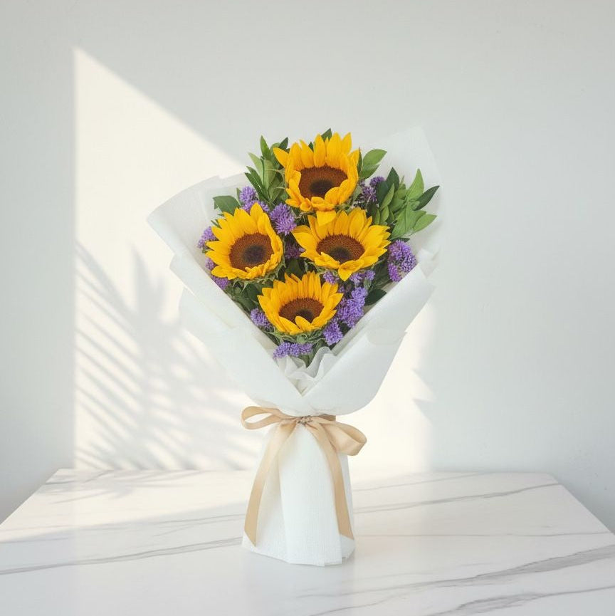 Bouquet of sunflowers and purple flowers in a white vase on a light surface with a white background