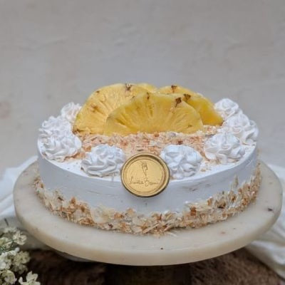 Cake with white frosting, pineapple slices, and a gold coin on a white background freshly baked cake delivered in mumbai