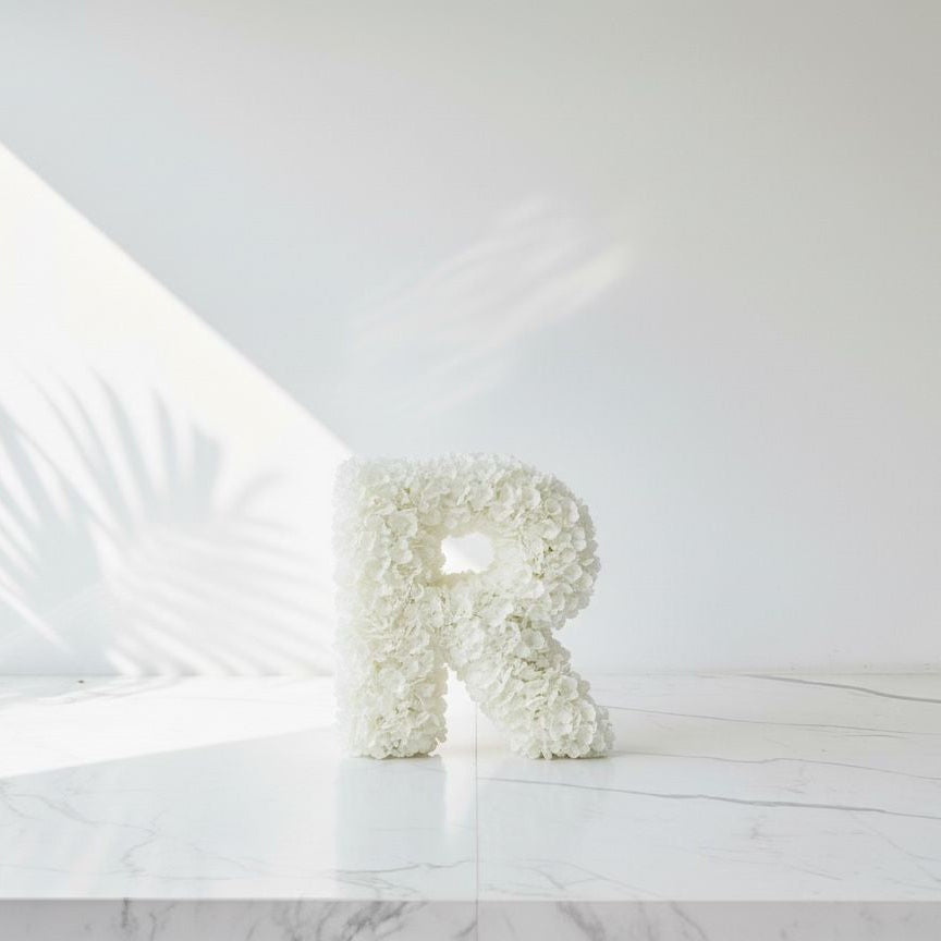 Floral letter 'R' on a white marble surface with a light gray background
