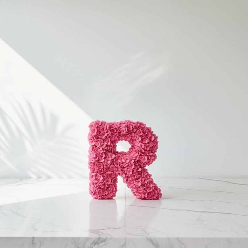 Pink letter 'R' made of flowers on a white marble surface