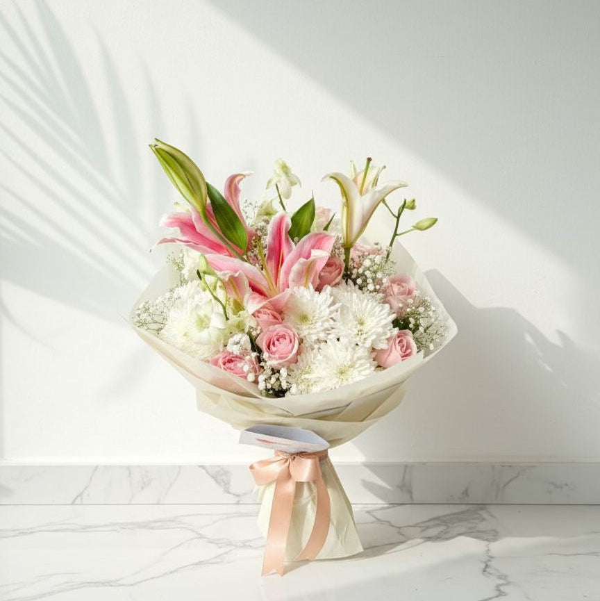 Bouquet with pink lilies, pink roses, white chrysanthemums, and baby’s breath wrapped in cream paper with a peach ribbon.