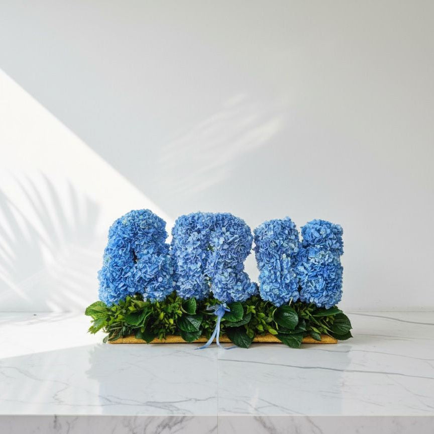 Blue floral arrangement spelling out 'LOVE' on a white marble surface.