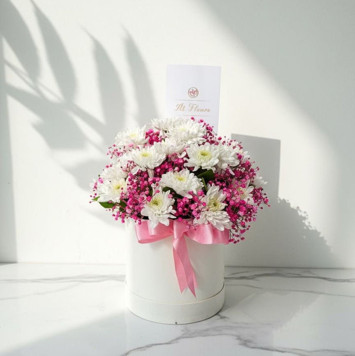 Bouquet of white and pink flowers in a white container with a pink ribbon on a marble surface. real flowers
