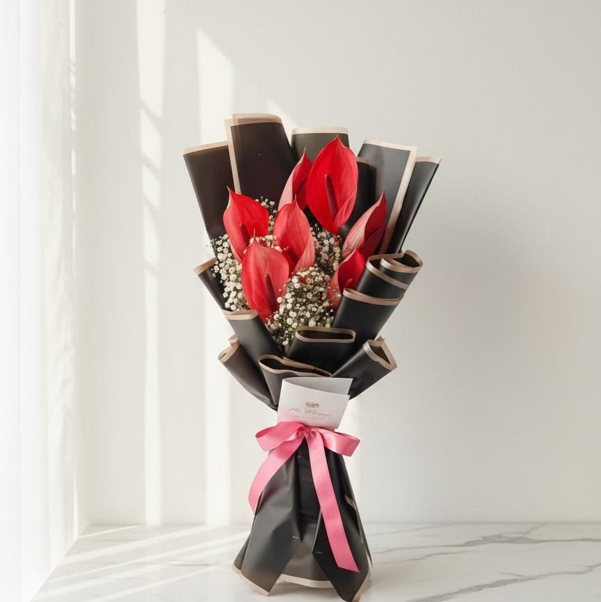 Red anthurium bouquet wrapped in black paper with baby’s breath and a pink ribbon.