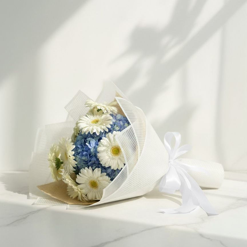 Bouquet of blue and white flowers wrapped in white paper with a ribbon on a white background