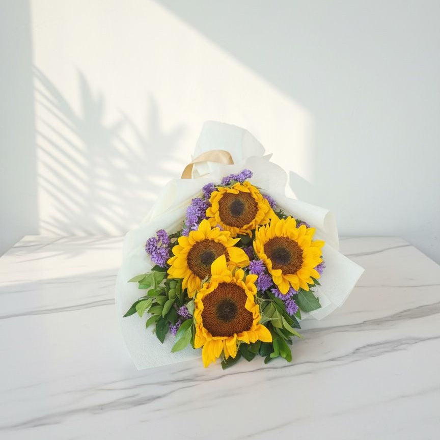 Bouquet of sunflowers and purple flowers on a white surface with a light gray background