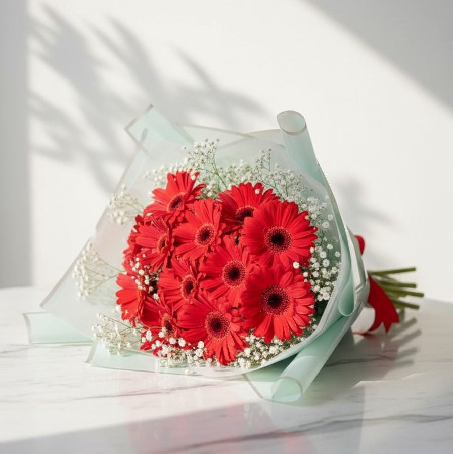 Bouquet of red flowers in a clear wrap on a white surface with light shadows.