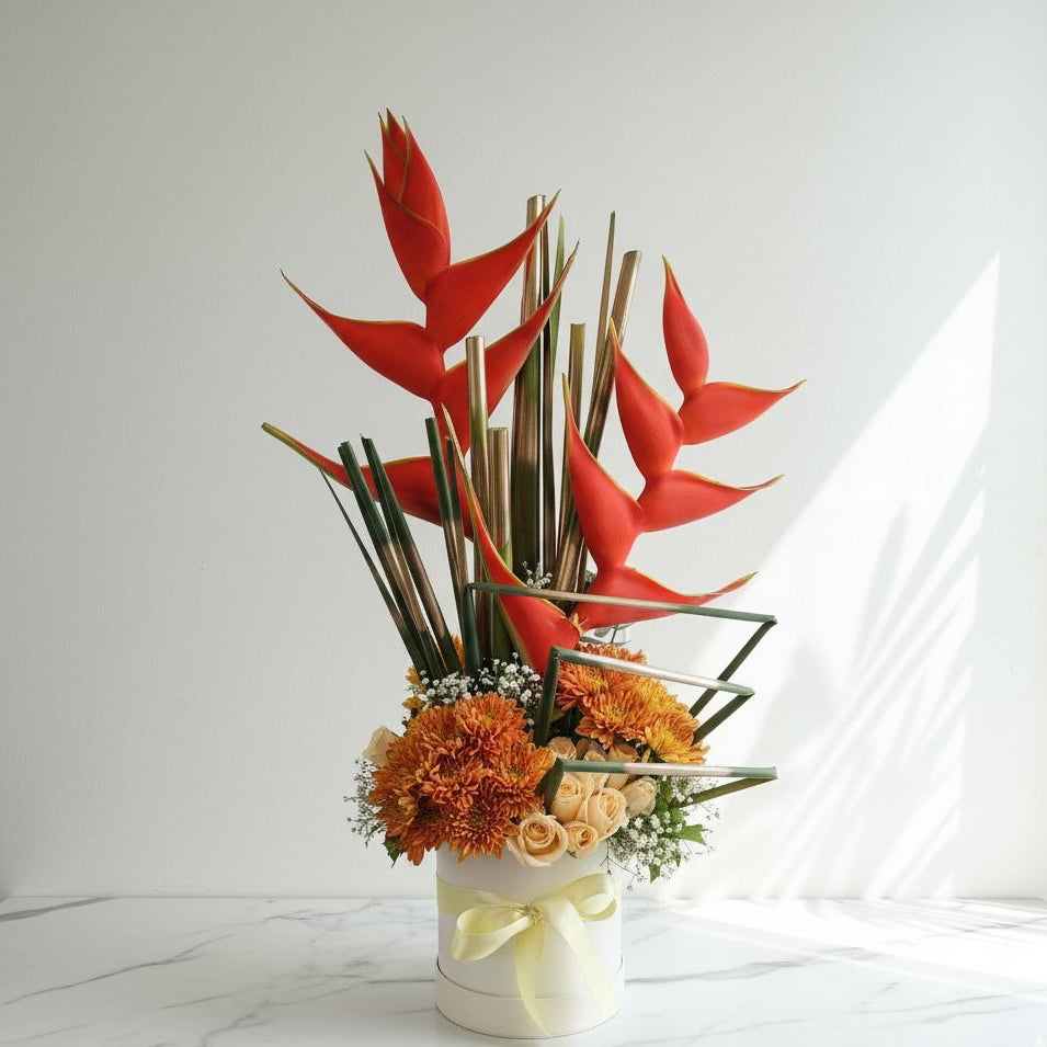 Floral arrangement with red heliconia and orange flowers in a white vase on a light background