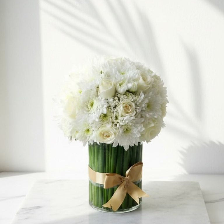 Floral arrangement in a green vase with a gold bow on a white surface fresh flowers 